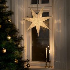 a lighted star hanging from the side of a window sill next to a christmas tree