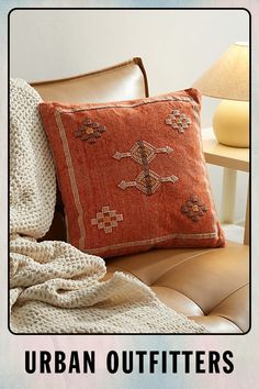 an orange pillow sitting on top of a brown leather chair next to a white blanket