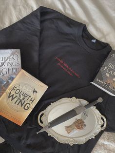 some books and a knife are laying on a bed with a black t - shirt