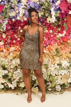 a woman standing in front of a flower wall wearing a gold sequined dress