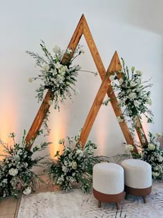 two stools with flowers and greenery on them in front of a white wall