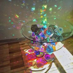 a glass table topped with lots of different colored pieces of art sitting on top of a wooden floor