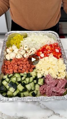 a person standing in front of a tray full of food that includes meat, cheese and vegetables