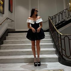 a woman in a black dress standing on the stairs with her hand on her hips