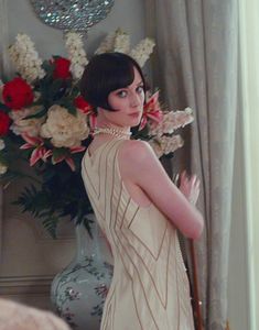 a woman standing in front of a vase with flowers on the wall and wearing a dress