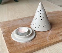 a small white candle holder sitting on top of a wooden cutting board next to a lit candle