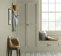 a room with a bench, coat rack and hat on the wall next to a window