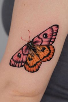 an orange and pink butterfly tattoo on the right arm, with black dots around it