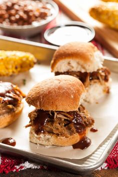 two pulled pork sandwiches with barbecue sauce on a tray next to corn in the background