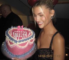 a woman is holding a birthday cake with candles on it and balloons in the background