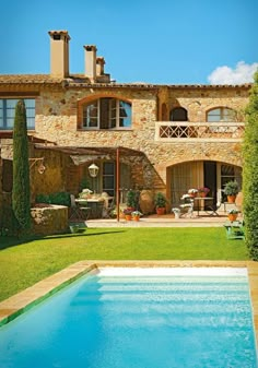 an outdoor swimming pool in front of a large stone house with two balconies