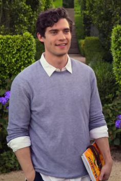 a man standing in front of some bushes holding a book and smiling at the camera