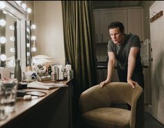 a man standing in front of a mirror next to a vanity with lights on it