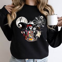 a woman is holding a cup and wearing a black sweatshirt with halloween characters on it