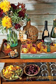 a wooden table topped with lots of bottles and glasses filled with liquid next to flowers