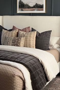 a large bed with many pillows on top of it next to a painting hanging above the headboard