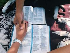 two people holding hands over an open book on the ground with grass in the background