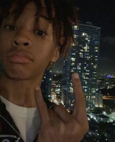 a man with dreadlocks making the peace sign in front of a cityscape