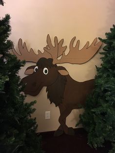 a moose is standing in front of some christmas trees and looking up at the ceiling