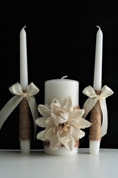 three white candles with burlocks and bows on them sitting next to each other