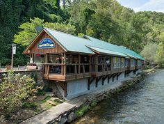 a restaurant on the side of a river with trees in the backgrouds