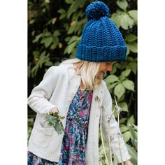 a woman wearing a blue knitted hat while walking through the woods with flowers in her hand