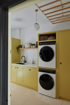 a kitchen with yellow cabinets and washer and dryer in the center, next to a sink