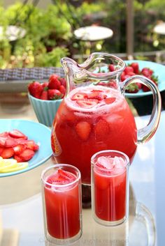 a pitcher of water with strawberries in it and three glasses filled with juice on the table