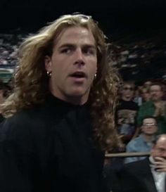 a man with long curly hair standing in front of an audience at a sporting event