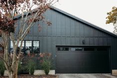 a black house with two garage doors and trees