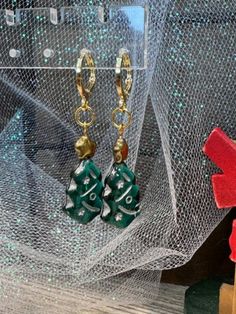 These delightful handmade dangle earrings are a festive addition to your holiday wardrobe. Featuring charming green Christmas tree charms adorned with gold stars, they evoke the magic of the season. Each earring is securely fastened with gold-plated round lever backs, ensuring comfort and elegance. Perfect for holiday parties or as a thoughtful gift, these earrings are a beautiful way to celebrate the joy of Christmas. Handmade Christmas Earrings For Celebration, Handmade Christmas Celebration Earrings, Handmade Festive Earrings For Christmas, Christmas Celebration Jewelry Drop Earrings, Christmas Celebration Drop Earrings Jewelry, Green Christmas Drop Earrings Jewelry, Green Holiday Earrings For Festive Occasions, Handmade Earrings For Holiday Celebrations, Christmas Celebration Dangle Earrings