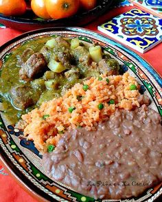 a plate with rice, beans and meat on it next to oranges in a bowl