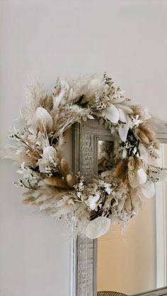 a wreath is hanging on the wall above a mirror with feathers and flowers around it