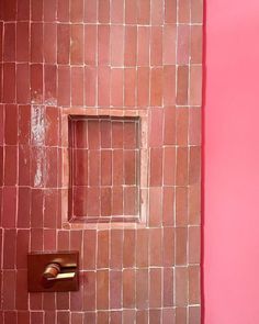 a pink tiled bathroom with a square hole in the wall and toilet paper dispenser