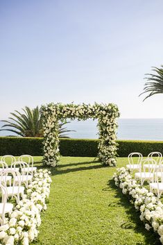 an outdoor ceremony set up with white flowers and greenery on the lawn next to the ocean