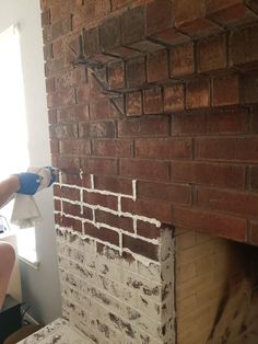 a brick fireplace being worked on by a person with blue gloves holding a rag over it