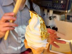 a person is holding an ice cream cone with gold foil on it and there is a machine in the background