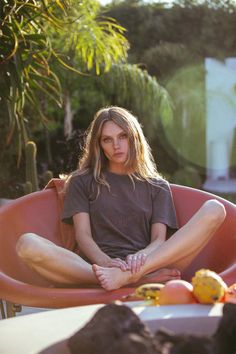 a woman sitting in a chair with fruit on the table next to her and looking at the camera