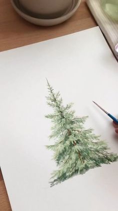 someone is drawing a christmas tree on paper with colored pencils and watercolor paints