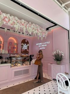 a woman standing in front of a pink bakery with white flowers hanging from the ceiling