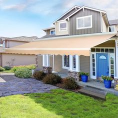 a house with an awning over the front door and landscaping around it, on a sunny day