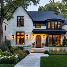 a white brick house with black trim and lights on it's windows, front steps leading up to the entryway