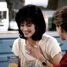 two women sitting at a table talking to each other in the middle of a kitchen