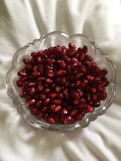 a glass bowl filled with pomegranate on top of a white cloth covered bed