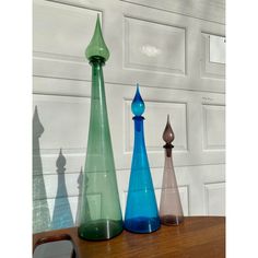 three different colored vases sitting on top of a wooden table next to a white wall