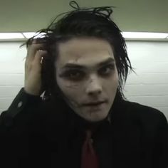 a man in a suit and tie with his hair pulled back, wearing black makeup