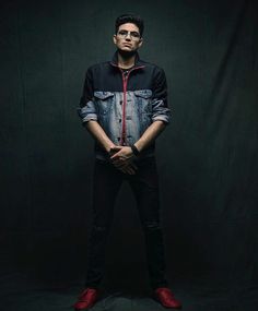 a man standing in front of a black background with his hands on his hips wearing red shoes