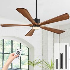 a person is holding a remote control in front of a ceiling fan with wooden blades