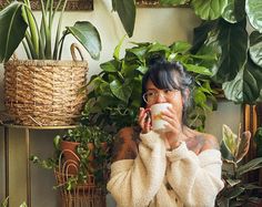 a woman is drinking from a cup in front of some potted plants