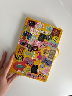 a person's hand holding onto a yellow notebook covered in stickers